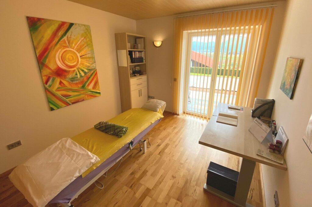 Der Massageraum von Tuina Praktiker Karrer mit einer Massageliege Schreibtisch und Bild an der Wand